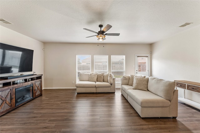 living room featuring visible vents, a textured ceiling, dark wood finished floors, and a ceiling fan