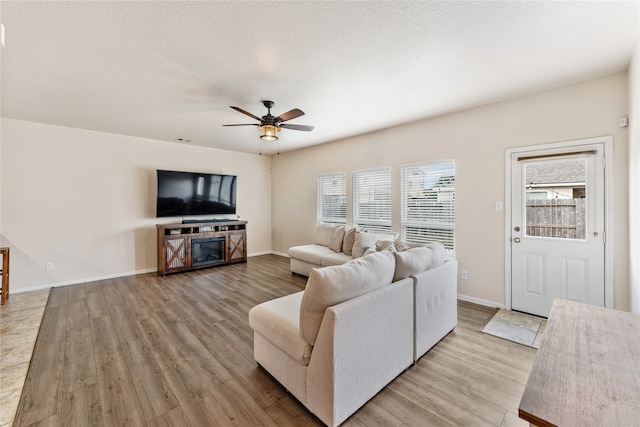 living area with a ceiling fan, baseboards, light wood finished floors, and a textured ceiling