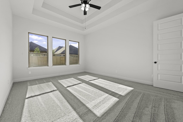 carpeted empty room with a raised ceiling and ceiling fan