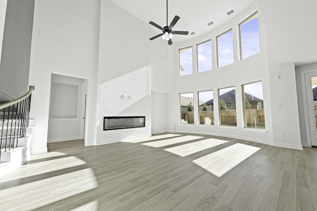 unfurnished living room featuring plenty of natural light, a large fireplace, light hardwood / wood-style floors, and a high ceiling