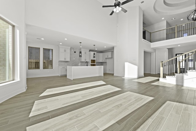 unfurnished living room featuring sink, ceiling fan with notable chandelier, light hardwood / wood-style floors, and a high ceiling