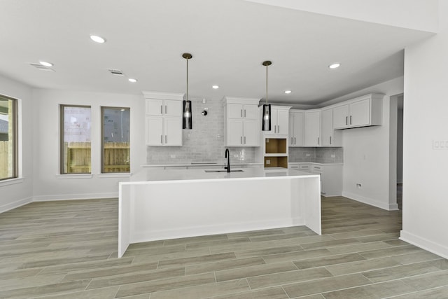 kitchen featuring a center island with sink, white cabinets, hanging light fixtures, and tasteful backsplash