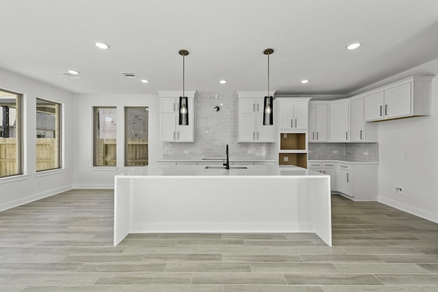 kitchen with backsplash, sink, pendant lighting, white cabinetry, and an island with sink