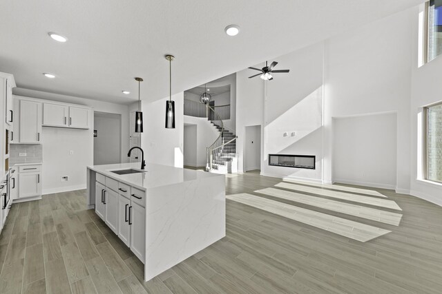 kitchen with white cabinets, pendant lighting, light stone counters, and sink