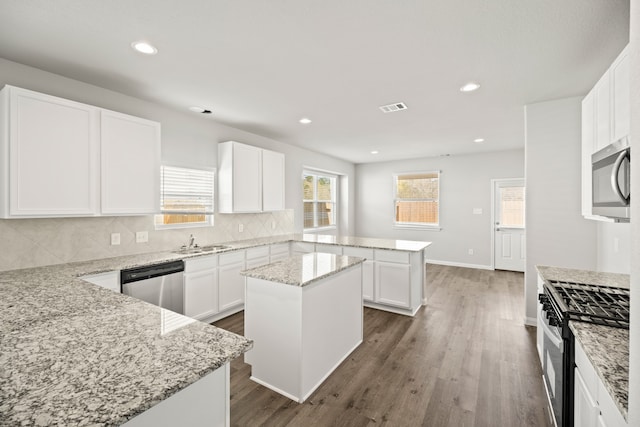 kitchen featuring light stone countertops, appliances with stainless steel finishes, a center island, white cabinets, and dark wood-type flooring