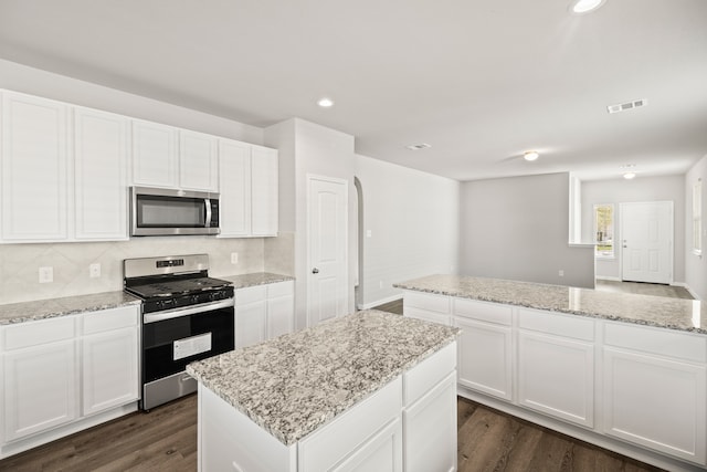 kitchen with appliances with stainless steel finishes, white cabinets, a center island, and dark hardwood / wood-style flooring