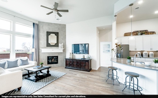 living area featuring a tiled fireplace, a ceiling fan, light wood-style flooring, and visible vents