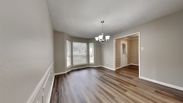 unfurnished dining area with hardwood / wood-style floors, a chandelier, and a textured ceiling