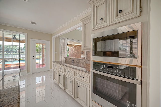 kitchen featuring stainless steel oven, stone counters, ornamental molding, built in microwave, and cream cabinetry