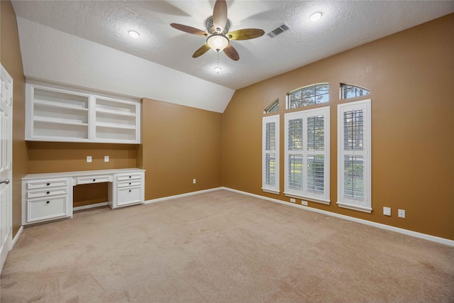 unfurnished office featuring visible vents, light carpet, built in study area, vaulted ceiling, and a textured ceiling