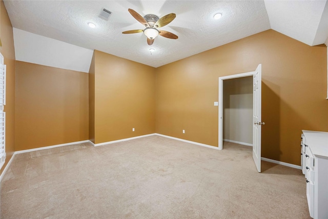 interior space featuring a textured ceiling, ceiling fan, vaulted ceiling, and light colored carpet