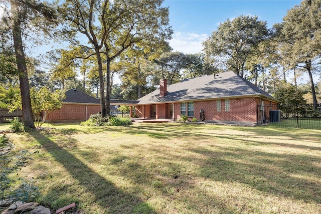 rear view of property featuring brick siding, a lawn, central AC unit, and fence