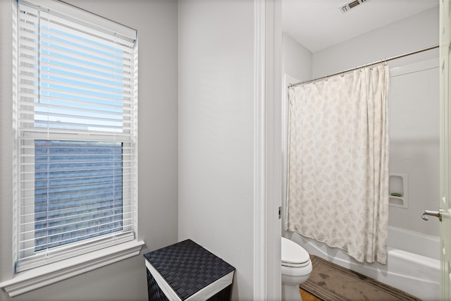 bathroom with shower / bath combination with curtain, toilet, and a healthy amount of sunlight