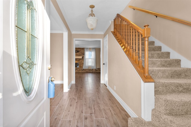 foyer entrance with hardwood / wood-style flooring, ornamental molding, and a brick fireplace