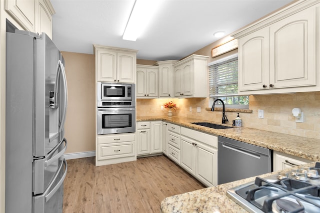 kitchen with tasteful backsplash, light stone countertops, appliances with stainless steel finishes, sink, and light hardwood / wood-style floors