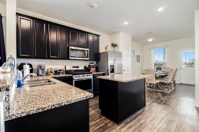 kitchen with a kitchen island, stainless steel appliances, sink, light stone countertops, and dark hardwood / wood-style flooring