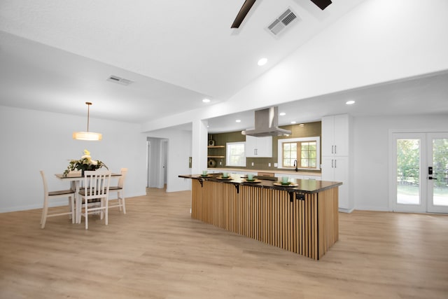 kitchen with pendant lighting, a breakfast bar, light hardwood / wood-style flooring, white cabinetry, and island exhaust hood