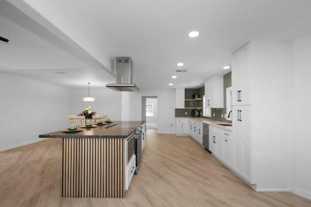 kitchen featuring light wood-type flooring, wall chimney range hood, a center island, white cabinetry, and hanging light fixtures