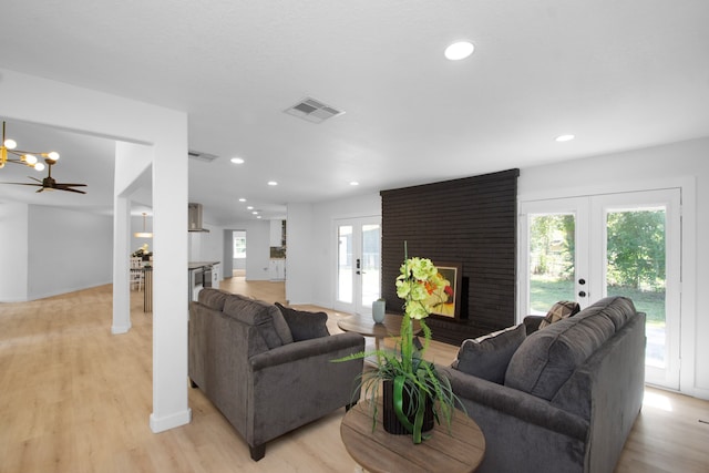 living room with a brick fireplace, ceiling fan, light wood-type flooring, and french doors