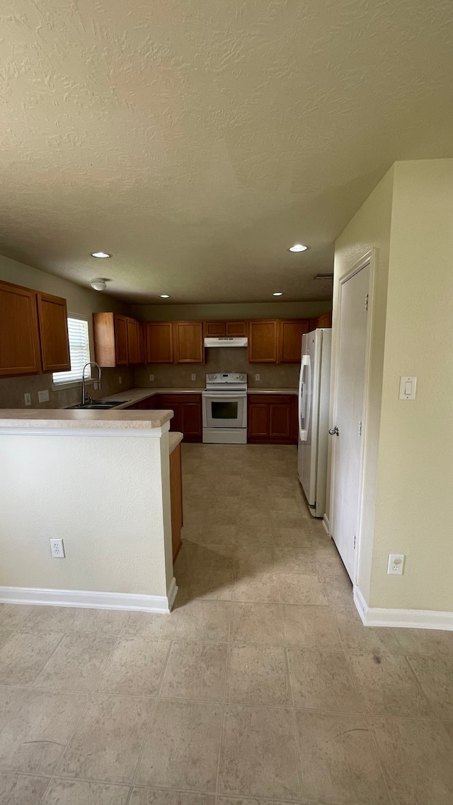 kitchen with white appliances, sink, a textured ceiling, kitchen peninsula, and light tile patterned floors