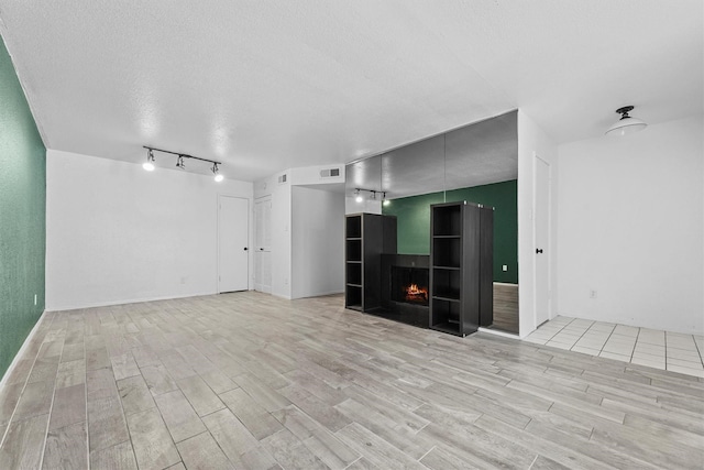 4643 Wild Indigo Unit 414, Houston, TX 77027 - unfurnished living room with a multi sided fireplace, light wood finished floors, a textured ceiling, and visible vents