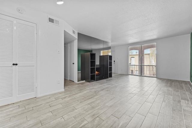 4643 Wild Indigo Unit 414, Houston, TX 77027 - unfurnished living room featuring visible vents, a textured ceiling, light wood-style flooring, and a fireplace