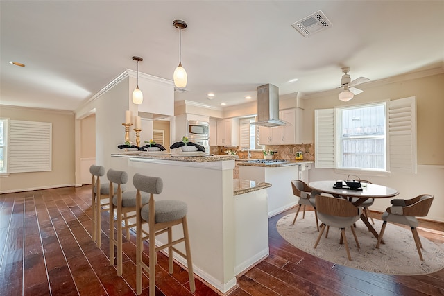 kitchen featuring range hood, dark wood-type flooring, stainless steel microwave, hanging light fixtures, and white cabinetry