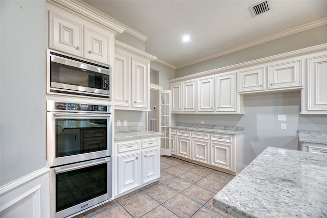 kitchen with appliances with stainless steel finishes, a textured ceiling, light tile patterned flooring, crown molding, and light stone counters