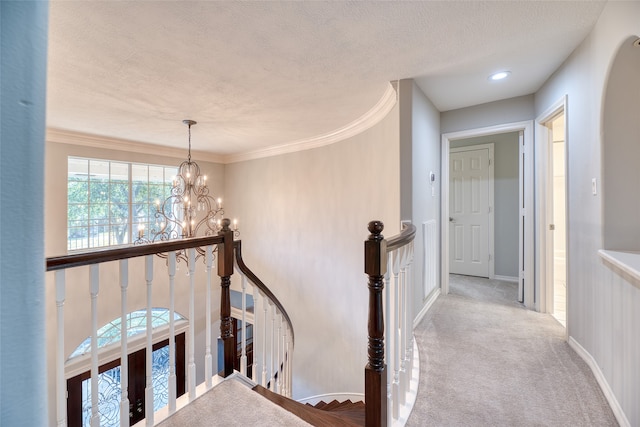 corridor with ornamental molding, light carpet, a textured ceiling, and an inviting chandelier