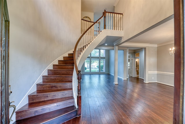 stairway with an inviting chandelier, crown molding, hardwood / wood-style floors, and a towering ceiling