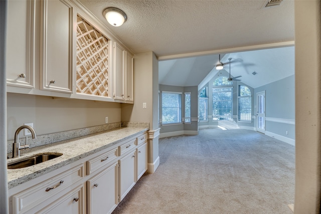 kitchen featuring sink, a textured ceiling, lofted ceiling, light stone counters, and light colored carpet