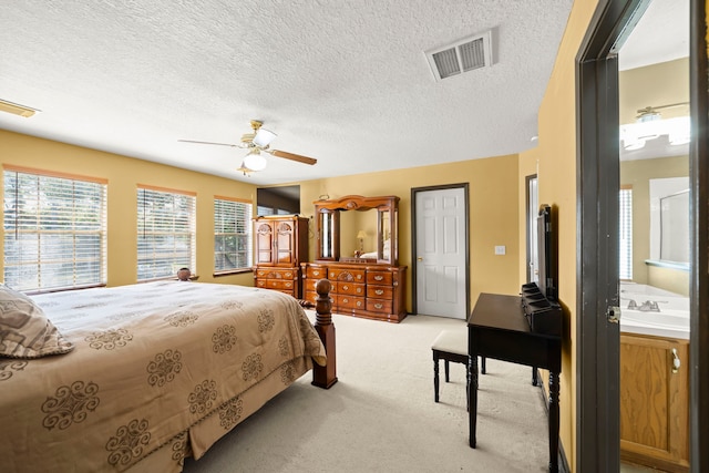 carpeted bedroom with a textured ceiling, ensuite bath, sink, and ceiling fan