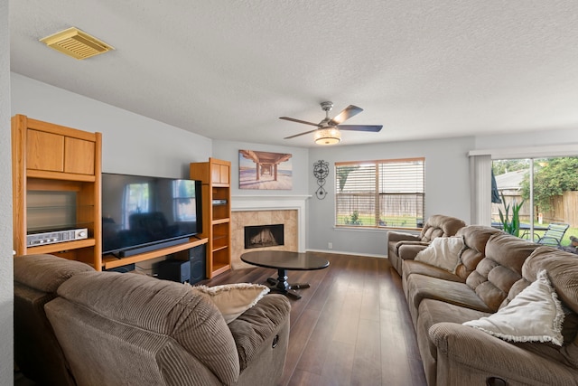 living room with a textured ceiling, ceiling fan, a tiled fireplace, and dark hardwood / wood-style flooring