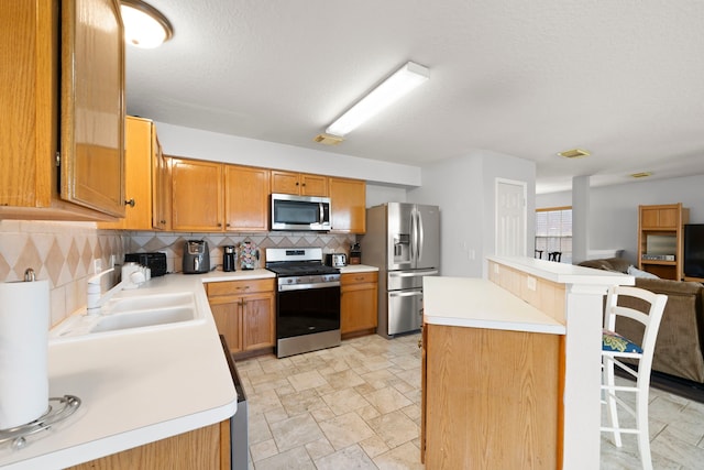 kitchen featuring tasteful backsplash, a breakfast bar area, a textured ceiling, sink, and stainless steel appliances