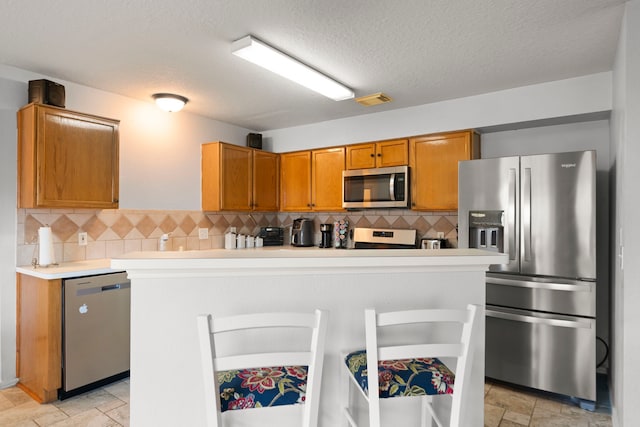 kitchen featuring a kitchen breakfast bar, appliances with stainless steel finishes, a textured ceiling, and tasteful backsplash