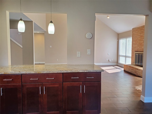 kitchen with light stone countertops, a brick fireplace, dark hardwood / wood-style floors, hanging light fixtures, and lofted ceiling