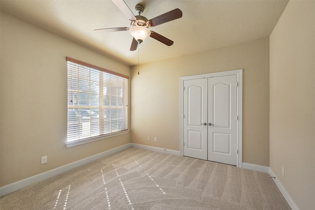 unfurnished bedroom featuring a textured ceiling, ceiling fan, light carpet, and a closet