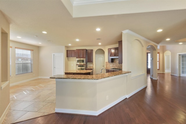 kitchen featuring appliances with stainless steel finishes, backsplash, light hardwood / wood-style floors, and dark stone countertops