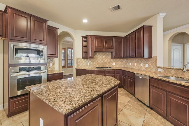 kitchen with light stone countertops, sink, stainless steel appliances, a kitchen island, and ornamental molding