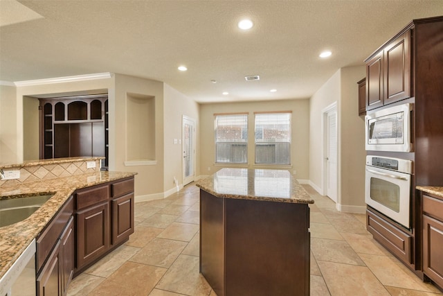 kitchen featuring backsplash, light stone counters, a textured ceiling, stainless steel appliances, and sink