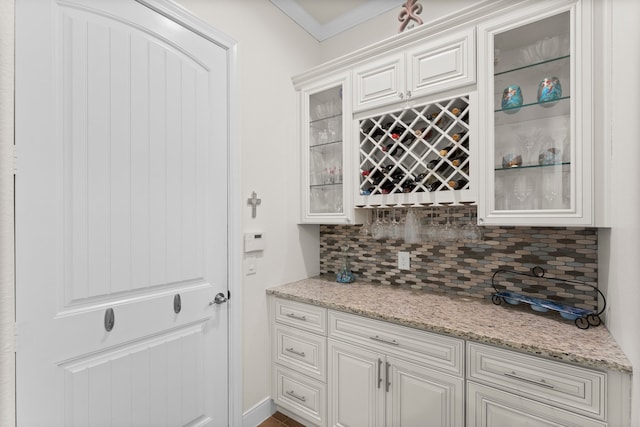 bar featuring decorative backsplash, white cabinetry, crown molding, and light stone counters