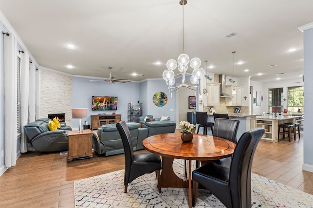 dining area with ornamental molding, light hardwood / wood-style flooring, ceiling fan, and a stone fireplace