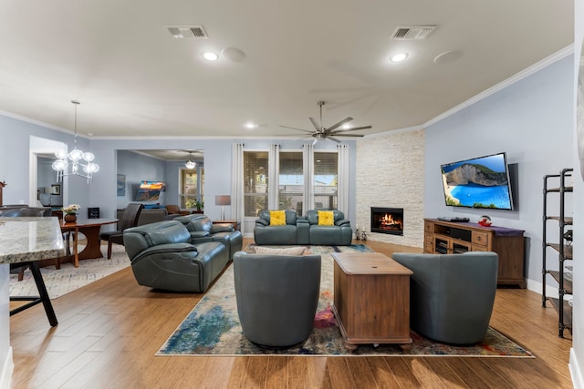 living room featuring hardwood / wood-style flooring, ceiling fan with notable chandelier, a stone fireplace, and crown molding