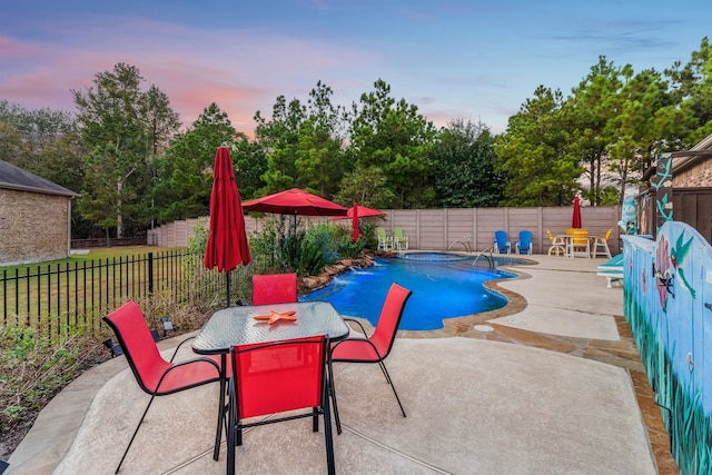 pool at dusk featuring a patio area and an in ground hot tub