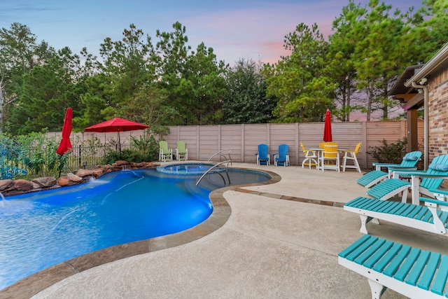 pool at dusk with pool water feature, a patio area, and an in ground hot tub