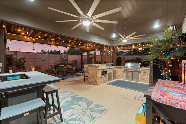 view of patio featuring a bar, an outdoor kitchen, grilling area, and ceiling fan