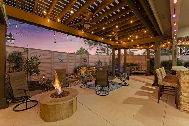 patio terrace at dusk with an outdoor bar, a pergola, and a fire pit