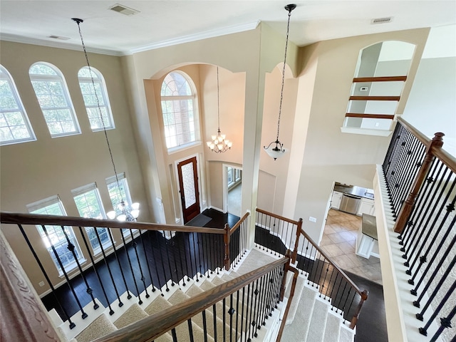 stairs with crown molding, an inviting chandelier, plenty of natural light, and carpet floors