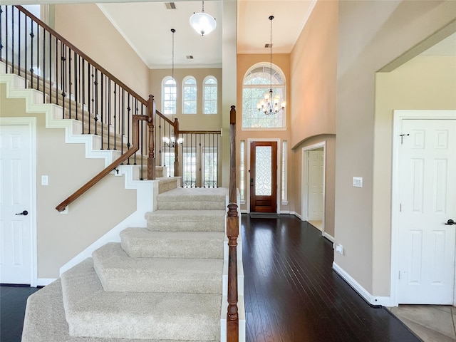 entryway with a towering ceiling, ornamental molding, a chandelier, and dark hardwood / wood-style floors