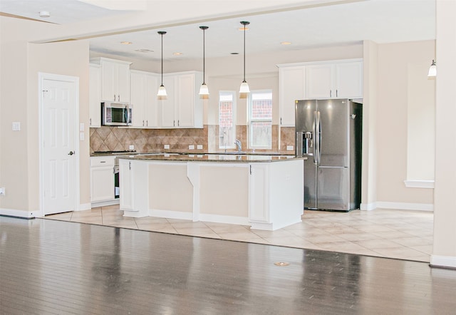 kitchen with a kitchen island, appliances with stainless steel finishes, white cabinetry, light wood-type flooring, and decorative light fixtures